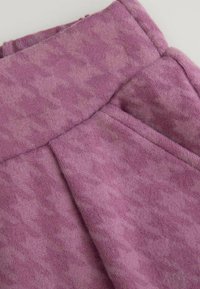 Fioletowy materiał polarowy o subtelnym wzorze w houndstooth i miękkiej fakturze, z widocznymi szwami i zagnieceniami.