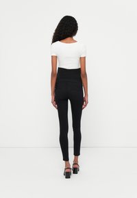 Jeans skinny de tiro alto en negro con bolsillos traseros, combinados con una blusa blanca de mangas cortas. Textura suave, diseño ajustado y longitud hasta el tobillo.
