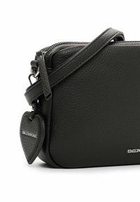 Borsa a tracolla in pelle nera texturizzata con chiusura a zip, caratterizzata da un'etichetta a forma di cuore e dettagli in metallo.