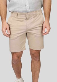 Shorts en coton beige avec une taille plate, des poches latérales et des ourlets retroussés, présentant une texture lisse et une coupe classique.