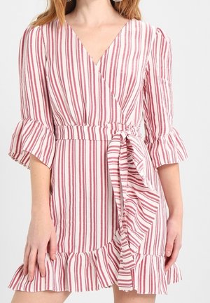 Femme portant une robe portefeuille à rayures verticales roses et blanches avec des manches et un ourlet à volants, nouée à la taille avec une ceinture assortie en tissu.