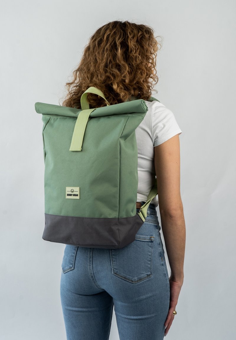 Zielony plecak typu roll-top z szarym dnem, wykonany z trwałego materiału. Posiada uchwyt u góry oraz regulowane paski, prosty design z logo marki.