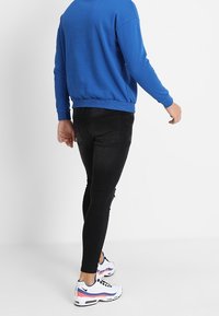 Sudadera azul con cuello redondo, jeans ajustados negros y zapatillas deportivas blancas con acentos rosas, vista desde la parte de atrás.