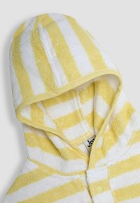Žlutý a bílý pruhovaný hřejivý plášť s kapucí vyrobený z měkké, strukturované tkaniny, s knoflíkovým zapínáním a žlutým lemováním kolem kapuce.