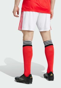 Rotes Sporttrikot mit weißen Shorts, schwarzen Fußballschuhen und roten, knielangen Socken mit schwarz-grauen Streifen oben.
