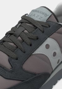 Adidașii Saucony Jazz au un amestec de suede gri închis și țesătură mov, cu un logo gri, șireturi texturate și o talpă din cauciuc.