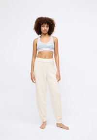 Αθλητική ριγέ κορυφή bralette σε ανοιχτό μπλέ, κόκκινο και λευκό. Κρεμ χρώματος, αφράτοι, ψηλόμεσοι παντελόνες φόρμας με ελαστική μπάσκα στους αστραγάλους.