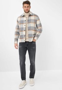 Giacca a quadri grigia e beige con bottoni, abbinata a un dolcevita chiaro e jeans scuri, con sneakers in pelle in un contesto informale.