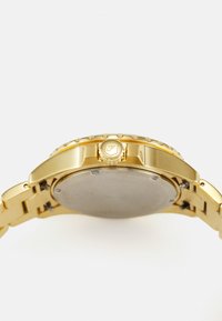 Montre-bracelet dorée avec un bracelet en acier inoxydable poli, une lunette texturée, une couronne proéminente et un boîtier rond et lisse.