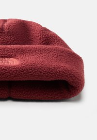 Gorro de fleece vermelho com dobra na bainha. O material é macio e texturizado, apresentando um logótipo subtil em relevo na parte da frente.