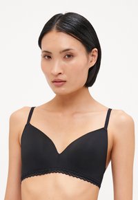Black bra with a smooth texture, underwire support, plunging neckline, and scalloped lace trim along the band. Adjustable thin straps.