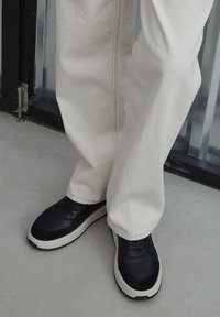 Černé kožené tenisky s texturovaným povrchem, bílou podrážkou a tkaničkami. Spárovány s volnými světle béžovými kalhotami.