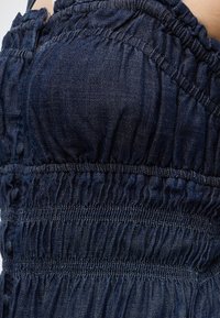 Κοντινή λήψη ενός σκουρόχρωμου μπλε denim ρούχου με μαζεμένες ελαστικές ραφές και ρυτιδωτή υφή.