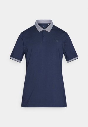 Tamsiai mėlyni polo marškinėliai trumpomis rankovėmis, kontrastingo rašto apykaklė, trijų mygtukų saga ir mažas logotipas ant krūtinės. Lygus audinys.