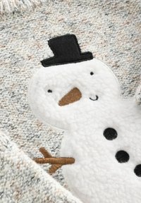 Pull en tricot texturé gris et crème. Présente une applique en peluche représentant un bonhomme de neige blanc avec un chapeau noir, un nez en carotte orange et des boutons noirs.