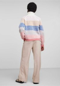 Stickad tröja med flerfärgade ränder i rosa, blått och beige. Den har en hög krage och en lös passform, i kombination med ljusbeiga vida byxor.