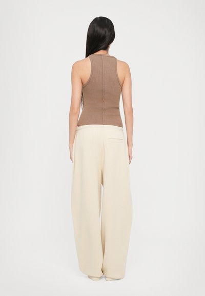 Pruun ribadega tank top, mis on sobitatud kreemjate laia säärtega pükste jaotusega. Topil on istuv disain, samas kui pükstel on mugav lõige ja küljetaskud.