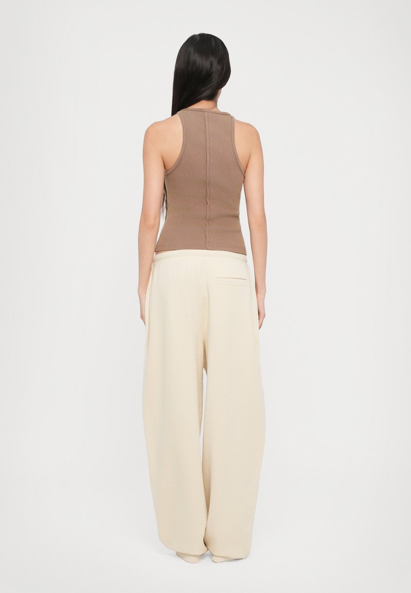 Brown ribbed tank top paired with cream wide-leg pants. The top features a fitted design, while the pants have a relaxed fit and side pocket.