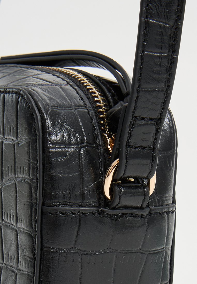 Schwarze Krokodilleder-Handtasche mit goldener Reißverschluss- und verstellbarem Riemen-Detail.