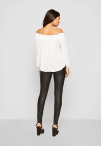 Witte off-the-shoulder top met geplooide halslijn en lange mouwen. Gecombineerd met zwarte neplederen legging, met een aansluitend ontwerp en hoge taille.