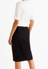 Weißes kurzärmeliges Oberteil, kombiniert mit einem enganliegenden schwarzen Bleistiftrock. Das Outfit zeichnet sich durch eine glatte Textur und eine strukturierte Silhouette aus, mit einer Nahtdetail auf der Rückseite.