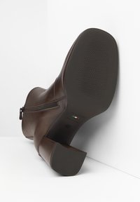 Bruine leren enkellaars met een ritsdetail, vierkante neus en chunky hak. Heeft een gestructureerde rubberen zool en branding op de zool.