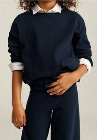Sudadera azul marino con textura acanalada, que presenta un escote redondo y un bolsillo. Combinada con pantalones azules marinos a juego para un look coordinado.