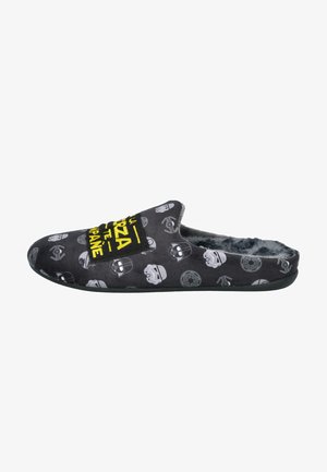 Pantufla de tela negra con interior de felpa, con patrones de calaveras en gris y blanco, y un gráfico de texto amarillo en la parte superior. Suela plana.