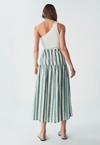 Asymetrický biely rebrovaný top spárovaný s tiered maxi sukňou so zelenými a bielymi pruhmi. Sukňa má voľný dizajn a elastický pás.