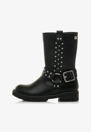 Botte de cheville en cuir noir avec une boucle, des détails de sangle cloutée et une semelle texturée. Fini lisse avec une forme cylindrique.