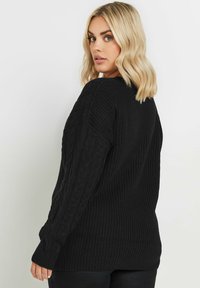 Musta palmikkoneule, jossa on tekstuuripinta ja pitkät hihat. Hihoissa ja helmassa on ribbireunat. Takapuoli on yksinkertainen ilman lisätietoja.