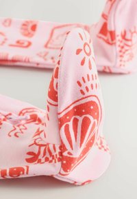 Tissu rose avec soleil rouge, coquillage et motifs abstraits, plié pour mettre en valeur le design imprimé détaillé sur un textile doux.