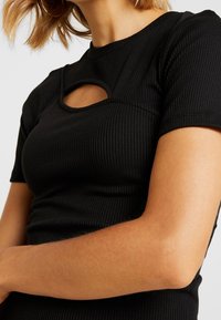 Svart ribbad t-shirt med kort ärm som har en rund hals med ett nyckelhålssnitt och en figurnära silhuett, som framhäver ett texturerat tyg.