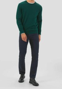 Groen langarmtrui met een ronde hals, gedragen over navy broek, in combinatie met zwarte veterschoenen. Zachte textuur, aansluitend ontwerp.