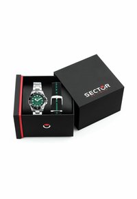 Orologio in metallo argentato con quadrante verde, cinturino in tessuto a strisce nere e verdi, esposto in una scatola nera con un logo rosso e bianco.