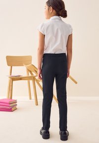 Camicia bianca a maniche corte con colletto abbinata a pantaloni neri slim-fit. Scarpe nere lucide completano l'outfit. Design minimalista, colori semplici.