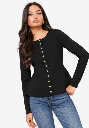 Mustast tekstuurkangast, pikemate varrukatega ja vormiva lõikega kardigan, mille esiküljel kuldsed nööbid. Kujunduses kõverdatud serv.