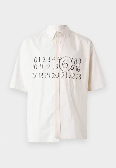 Κοντομάνικο πουκάμισο σε ανοιχτό μπεζ βαμβάκι με γιακά που κλείνει με κουμπί, διακοσμημένο με εκτυπωμένους μαύρους αριθμούς και κυκλικό στοιχείο στο κέντρο.