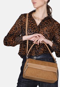 Tan suède handtas met een glad leren accent, ritssluiting, korte handgreep en afneembare schouderband. Over het geheel een rechthoekige vorm.