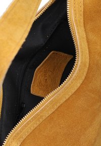 Suède handtas in mosterdgeel met een gouden ritssluiting en een zwarte stoffen voering. Inclusief een klein ritsvakje en een leren label aan de binnenkant.