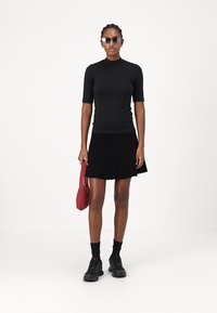 Top nero a maniche corte abbinato a una gonna nera, completato da sneakers nere texturizzate e una piccola borsa rossa. Inclusi occhiali da sole regolabili.