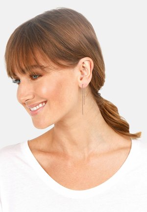 Pendientes largos y delgados de metal con un diseño elegante y minimalista y un acabado brillante, que cuelgan por debajo del lóbulo de la oreja.