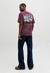 T-shirt graphique bordeaux avec le texte "WHISTLER" et un motif de montagne au dos, associé à un jean bleu foncé et des bottes marron.