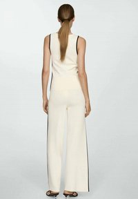 Cream-colored knit tank top and wide-leg pants; features black side stripes, smooth texture, and a fitted design.
