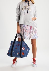 Sudadera gris con el texto "Keep Love", falda de estampado y bolsa de mezclilla con parches coloridos. Zapatillas blancas con cordones rojos.