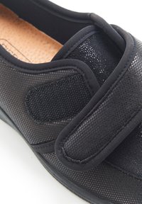 Scarpa nera senza lacci con tomaia in mesh testurizzato, imbottitura morbida e cinturino in Velcro. Presenta una punta arrotondata e un design minimalista.