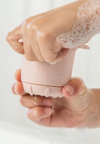 Zijdezachte roze siliconen zeepdispenser; voorzien van een textuurrijke grip, een cirkelvormig ontwerp en afwateringsgaatjes aan de onderkant, met zichtbare bellen op het oppervlak.