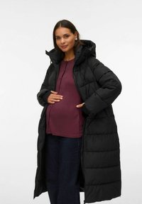 Melnā mīkstajā virsjaka ar kapuci, ar garu dizainu, ar rāvējslēdzēja kabatām un quilted tekstūru, valkāta virs bordo augšdaļas un džinsiem.