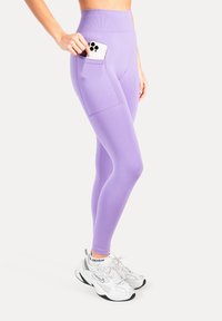 Lyse lilla leggings med høj talje og sidelomme, lavet af elastisk stof. Kombineret med hvide sneakers med sorte detaljer.