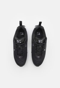 Black sneakers with textured fabric, round toe shape, white midsole, and prominent Nike logo on the tongue and side.